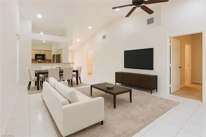 Virtually staged living room featuring high vaulted ceiling, light tile patterned flooring, recessed lighting, and a ceiling fan