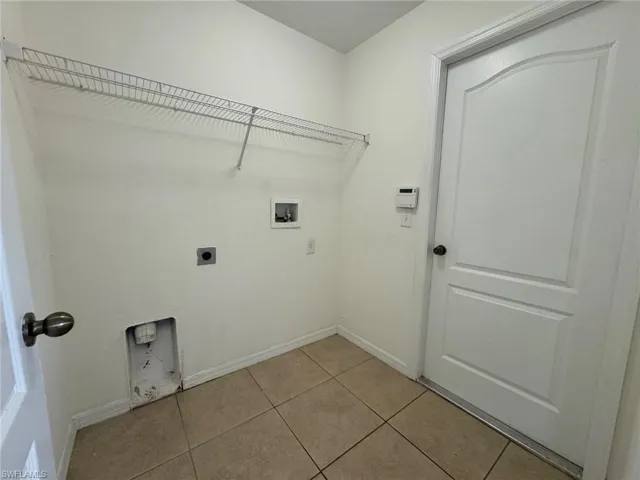 Washroom with light tile patterned floors, hookup for a washing machine, hookup for an electric dryer, laundry area, and baseboards