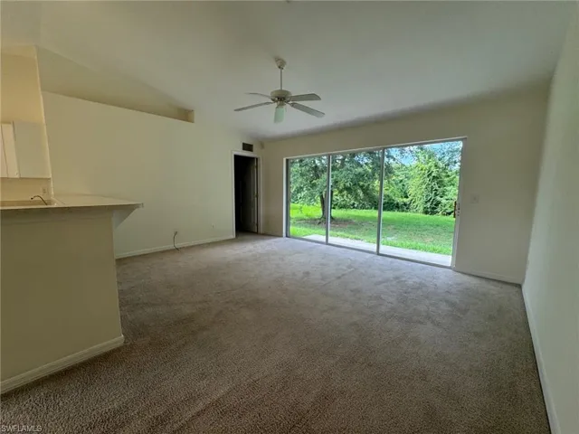 Unfurnished living room featuring lofted ceiling, baseboards, a ceiling fan, and light colored carpet