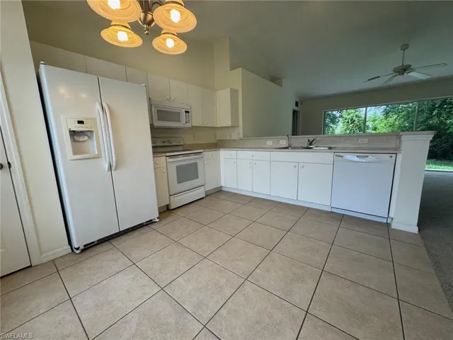 Kitchen with white appliances, light tile patterned floors, white cabinetry, and a sink