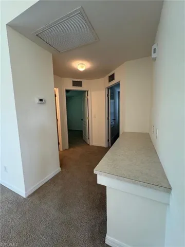 Hallway with baseboards, visible vents, and dark colored carpet