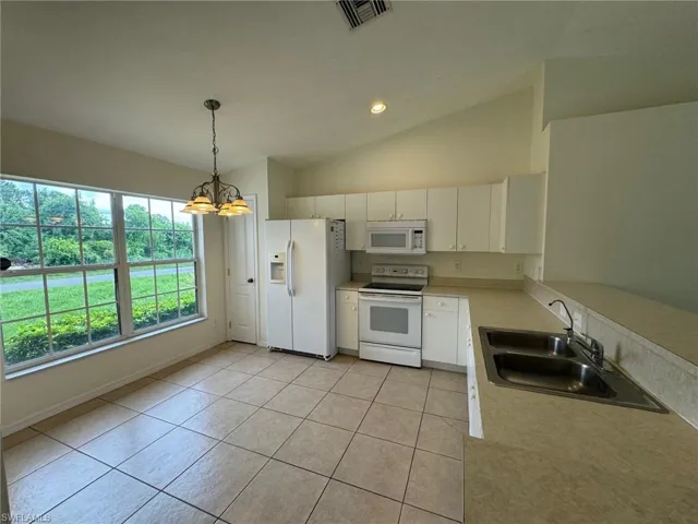 Kitchen featuring white appliances, a sink, visible vents, vaulted ceiling, and light countertops