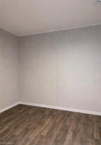 Empty room featuring dark wood-type flooring and baseboards
