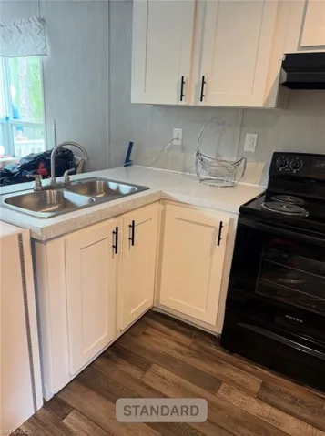 Kitchen featuring black range with electric cooktop, white cabinetry, light countertops, a peninsula, and dark wood-style flooring