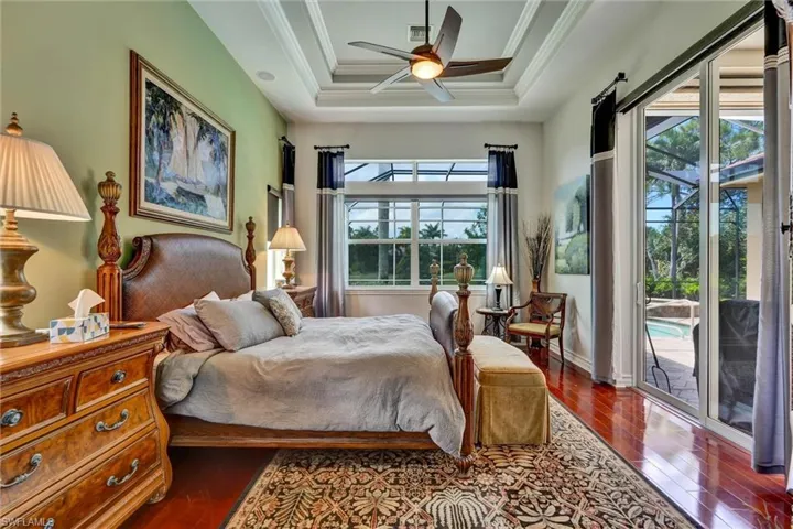 Spacious interior featuring rich wood-finish flooring, a multi-tiered tray ceiling with a built-in fan, and large windows with transom panels
