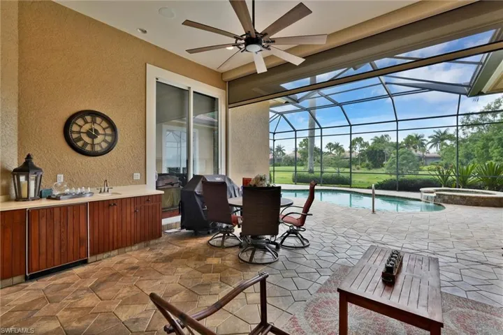 Screened outdoor living area featuring a built-in outdoor kitchen with sink, stone countertop, and wood-finish cabinetry