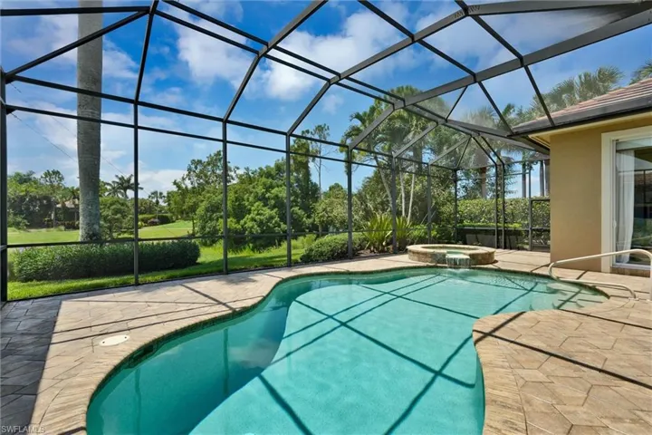 Screened lanai featuring a freeform swimming pool, integrated spa with waterfall feature, and textured paver decking