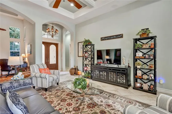 Living area featuring light-toned tile flooring, a tray ceiling with a ceiling fan, and arched doorways
