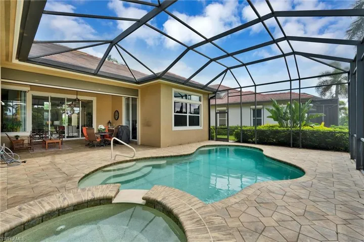 Screened lanai featuring a freeform pool, integrated spa, and extensive paver patio