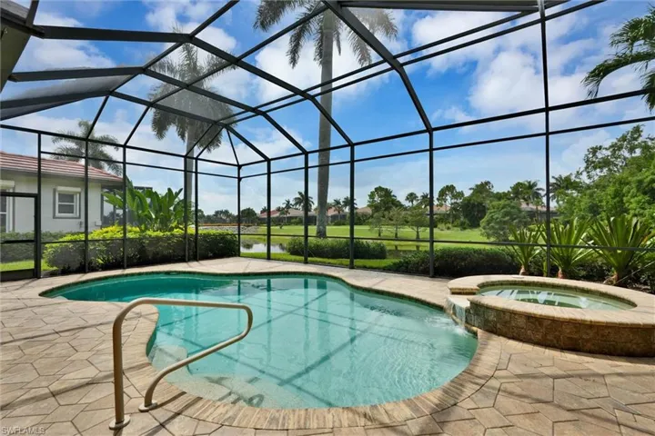 Screened-in outdoor pool area featuring a freeform swimming pool, integrated spa with waterfall feature, and surrounding paver patio