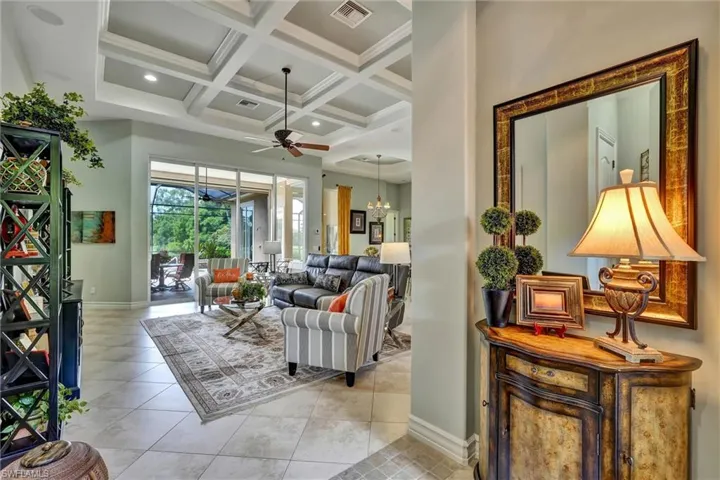 Spacious interior featuring coffered ceilings with recessed lighting and a ceiling fan, large format tile flooring, and broad sliding glass doors opening to an outdoor screened patio