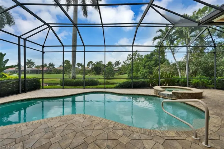 Screened lanai featuring a free-form swimming pool with integrated spa and stone surround
