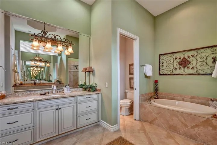 Spacious bathroom featuring an expansive vanity with double sinks and stone countertop, a large soaking tub with tiled surround, and separate water closet