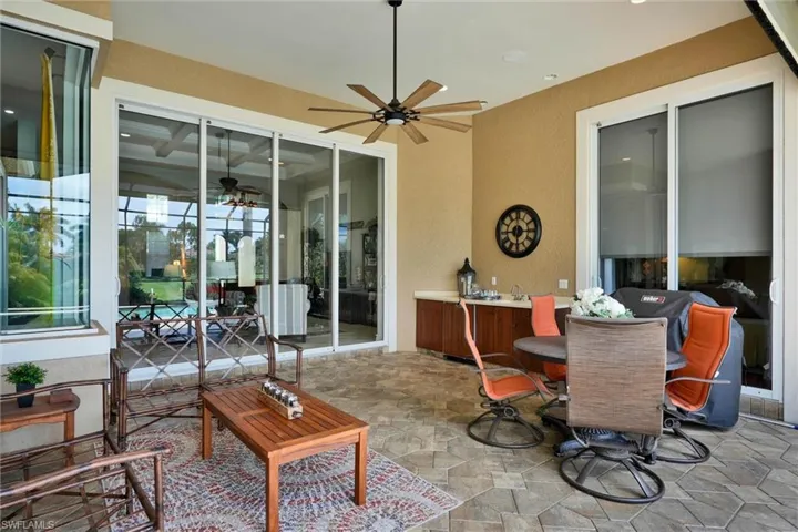 Expansive outdoor living area featuring textured tile flooring, an outdoor ceiling fan, and built-in cabinetry with a sink