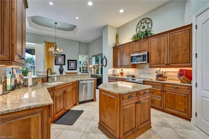 Gourmet kitchen featuring wood cabinetry, granite countertops, tile flooring, a central island, and stainless steel appliances
