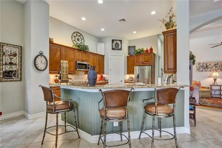 Open-concept kitchen featuring a multi-level breakfast bar with beadboard paneling, recessed lighting, wood cabinetry, stainless steel appliances, and tile flooring