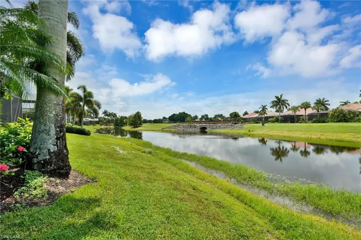 Waterfront setting featuring a stone bridge, lush green landscaping, and mature palm trees