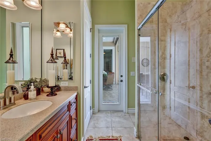 Bathroom featuring a glass-enclosed shower with tile surround, a single vanity with wood cabinetry and an integrated sink, and tile flooring