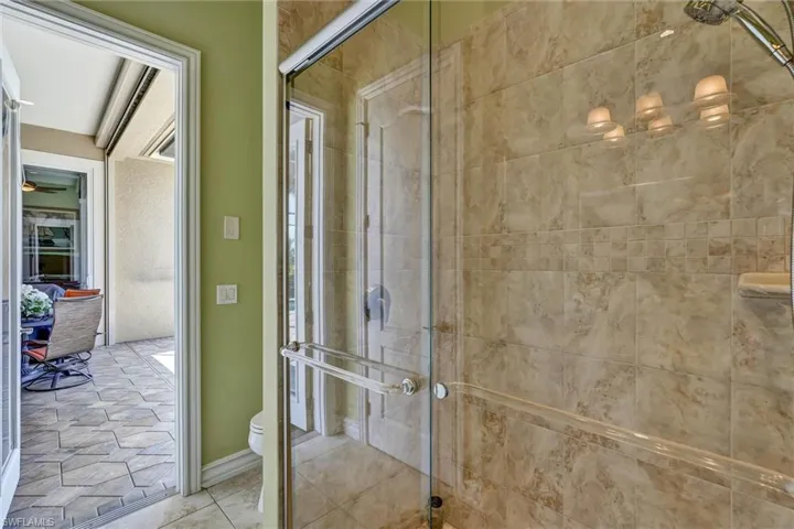 Glass-enclosed shower featuring large format natural stone-finish wall tiles with a decorative accent band, and a chrome shower fixture