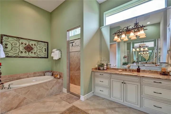 Spacious bathroom featuring a built-in tub, separate glass-enclosed shower, large vanity with dual sinks, extensive countertop space, and a high transom window