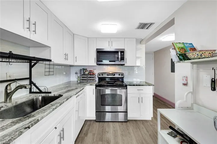Kitchen featuring light wood-type flooring, white cabinets, stainless steel appliances, decorative backsplash, and sink