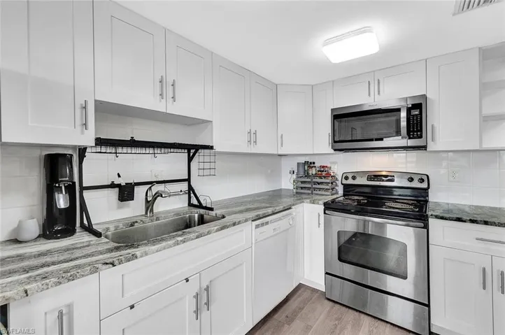 Kitchen featuring white cabinetry, stainless steel appliances, light wood-type flooring, light stone countertops, and backsplash