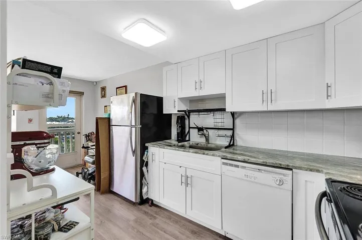Kitchen featuring white cabinetry, white dishwasher, light stone counters, light hardwood / wood-style flooring, and backsplash