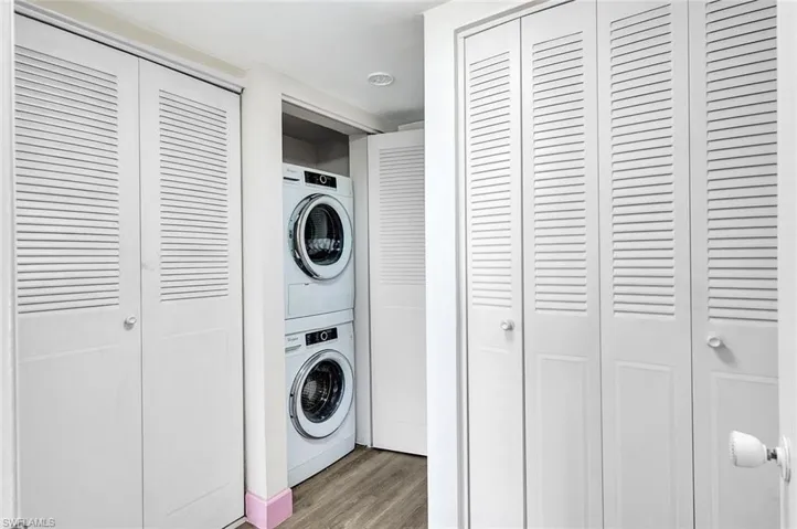 Laundry area with stacked washer and clothes dryer and wood-type flooring