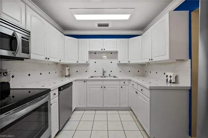 Kitchen featuring appliances with stainless steel finishes, light tile patterned floors, decorative backsplash, and sink