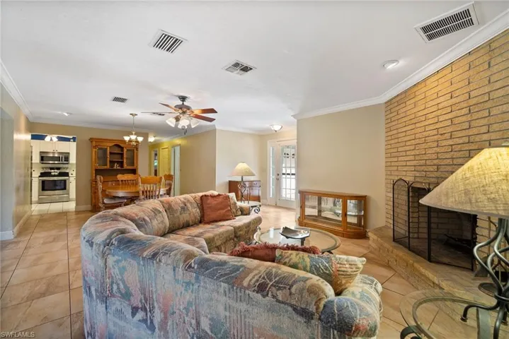 Living room featuring ceiling fan with notable chandelier, a brick fireplace, light tile patterned floors, and ornamental molding