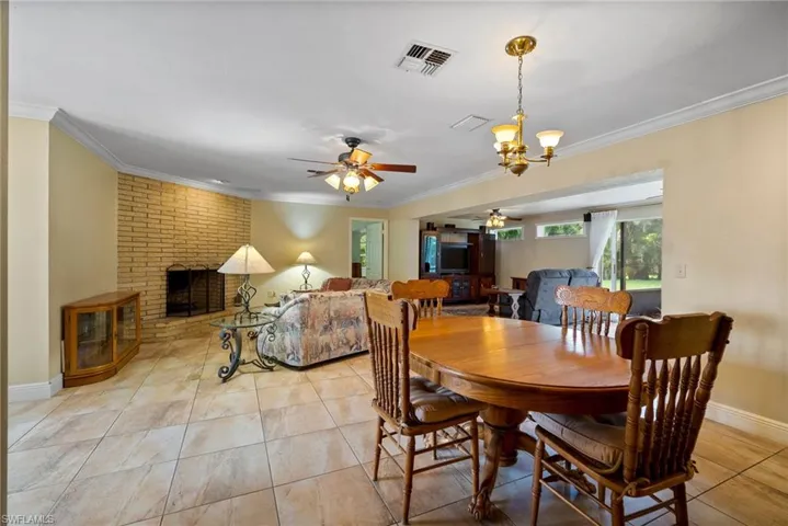 Dining space featuring crown molding, ceiling fan with notable chandelier, a brick fireplace, and light tile patterned floors