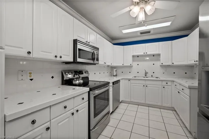 Kitchen featuring light tile patterned flooring, tasteful backsplash, ceiling fan, sink, and appliances with stainless steel finishes