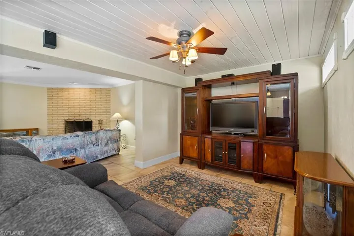 Living room with a fireplace, light tile patterned floors, brick wall, ceiling fan, and ornamental molding