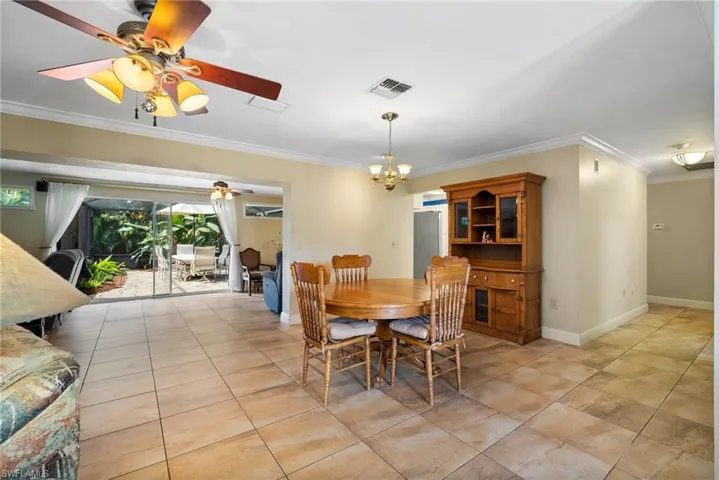 Dining area featuring ceiling fan with notable chandelier, crown molding, and light tile patterned floors