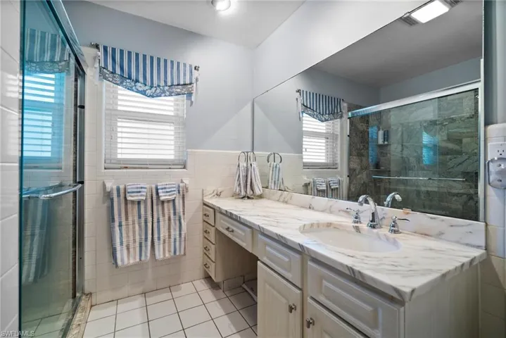 Bathroom with vanity, a shower with door, tile patterned flooring, and tile walls