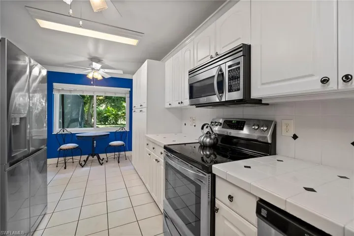 Kitchen featuring ceiling fan, stainless steel appliances, decorative backsplash, white cabinets, and tile counters