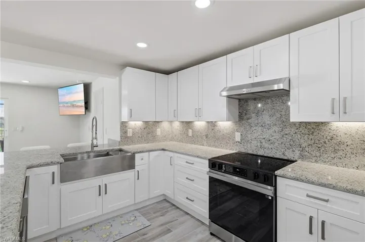Kitchen featuring range with electric cooktop, light stone countertops, under cabinet range hood, white cabinets, and recessed lighting
