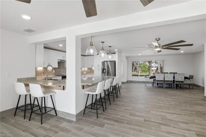 Kitchen featuring a breakfast bar, a peninsula, wood tiled floors, light stone countertops, and ceiling fan