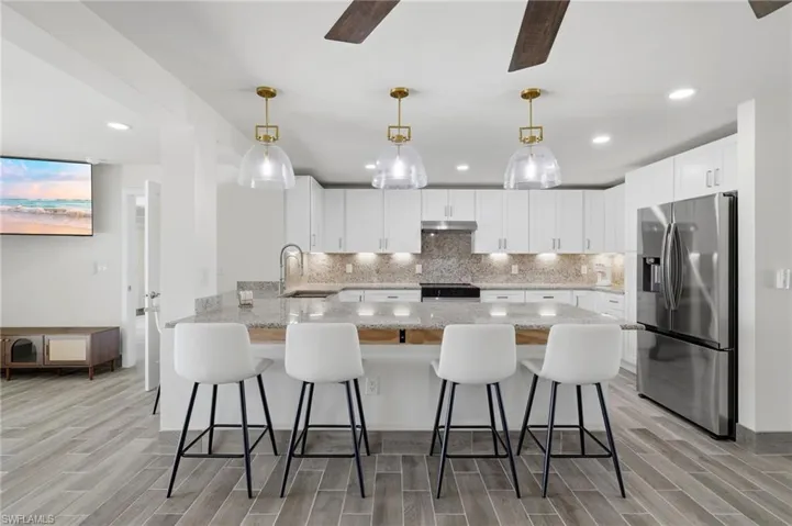Kitchen with a peninsula, wood tiled floors, a kitchen breakfast bar, stainless steel fridge with ice dispenser, and recessed lighting