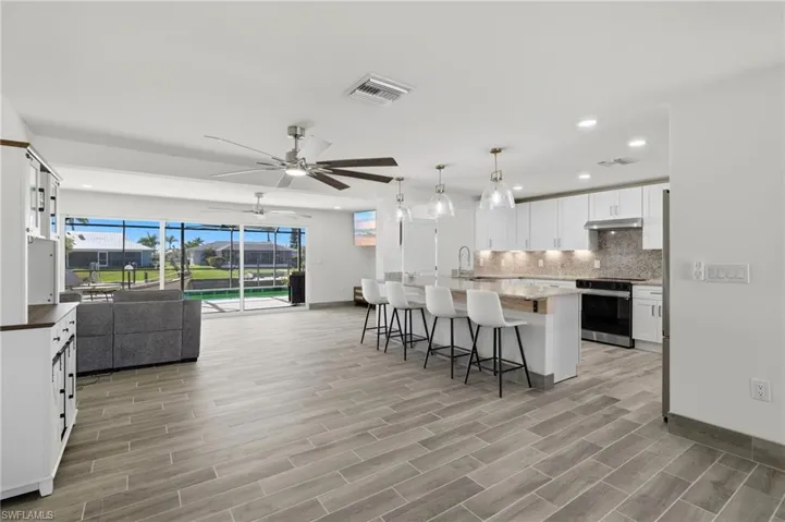 Kitchen with open floor plan, white cabinets, a breakfast bar area, backsplash, and a center island with sink