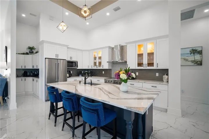 Kitchen with white cabinets, an island with sink, wall chimney range hood, and appliances with stainless steel finishes