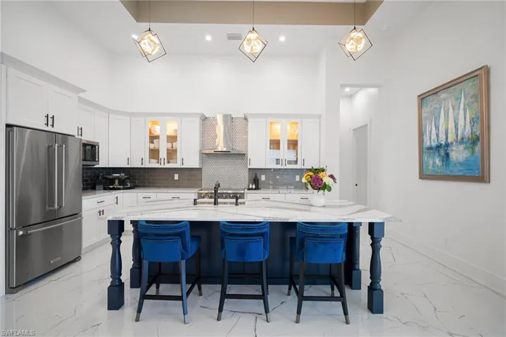 Kitchen with appliances with stainless steel finishes, white cabinetry, wall chimney exhaust hood, and an island with sink