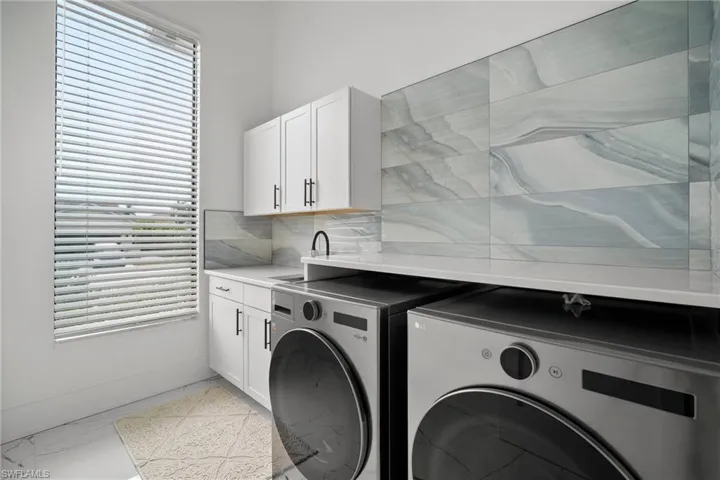 Clothes washing area featuring cabinets, washer and clothes dryer, and a healthy amount of sunlight