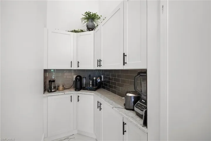 Bar with white cabinets, light stone countertops, and tasteful backsplash