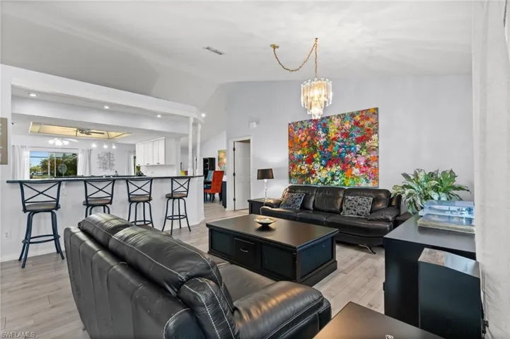 Living room featuring suspended lighting, light wood-style flooring, and vaulted ceiling