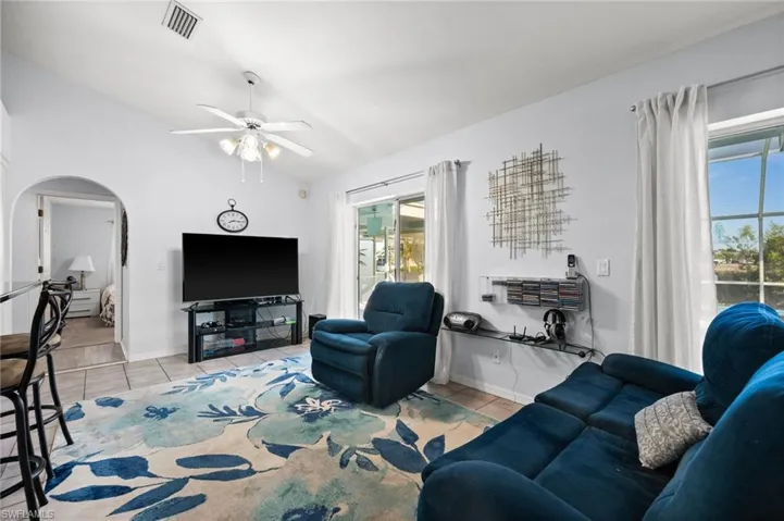 Living area with vaulted ceiling, light tile patterned floors, arched walkways, and ceiling fan