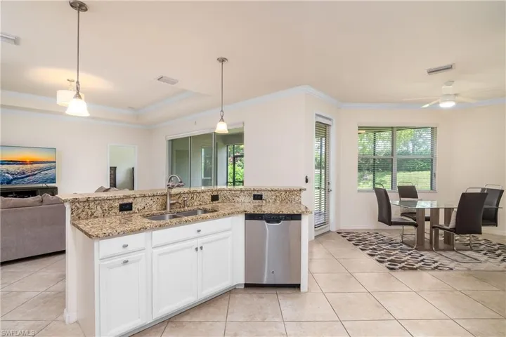 Kitchen featuring a tray ceiling, stainless steel dishwasher, light tile flooring, pendant lighting, and sink