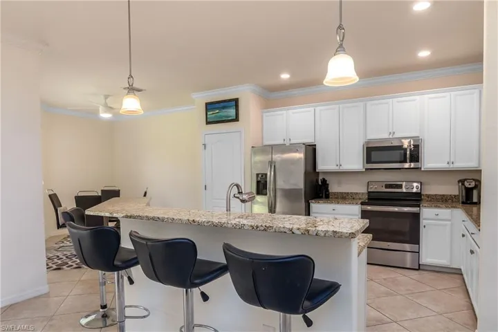 Kitchen with stainless steel appliances, decorative light fixtures, light tile floors, and a kitchen island with sink