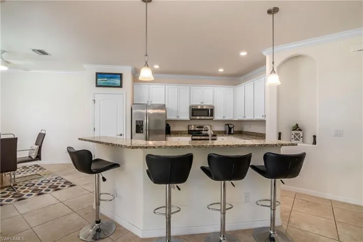 Kitchen with hanging light fixtures, light tile floors, white cabinetry, and appliances with stainless steel finishes