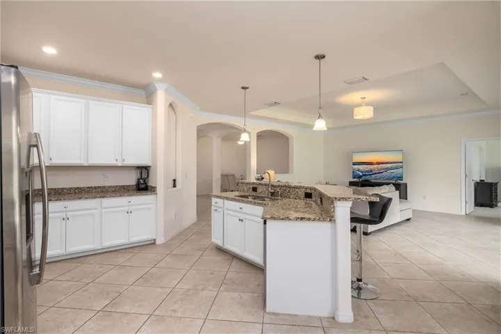 Kitchen featuring sink, stainless steel fridge with ice dispenser, a raised ceiling, and a breakfast bar